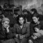Women and children sitting closely together in a worn shelter with distressed expressions