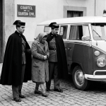 Two Guardia Civil officers in uniform escorting a woman detainee beside a police van